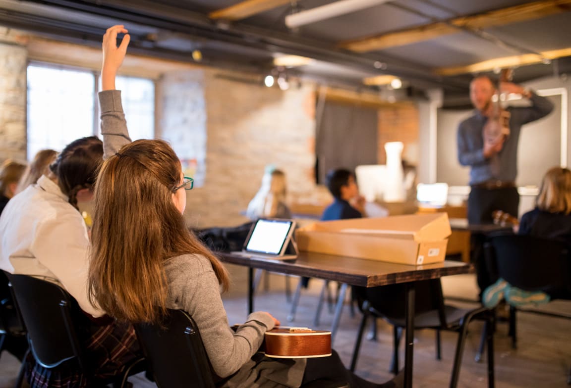 Picture of a student rasing their hand in a classroom full of students.