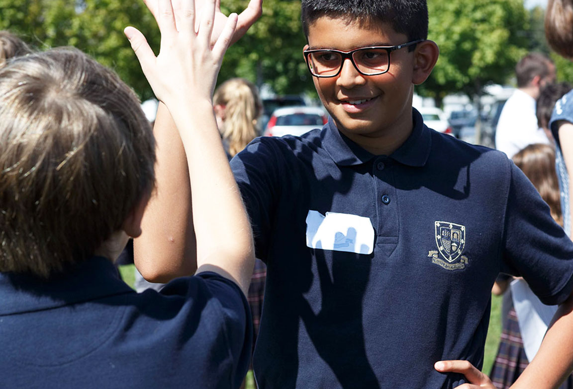 Picture of two students giving each other a high five outdoors during a school activity.