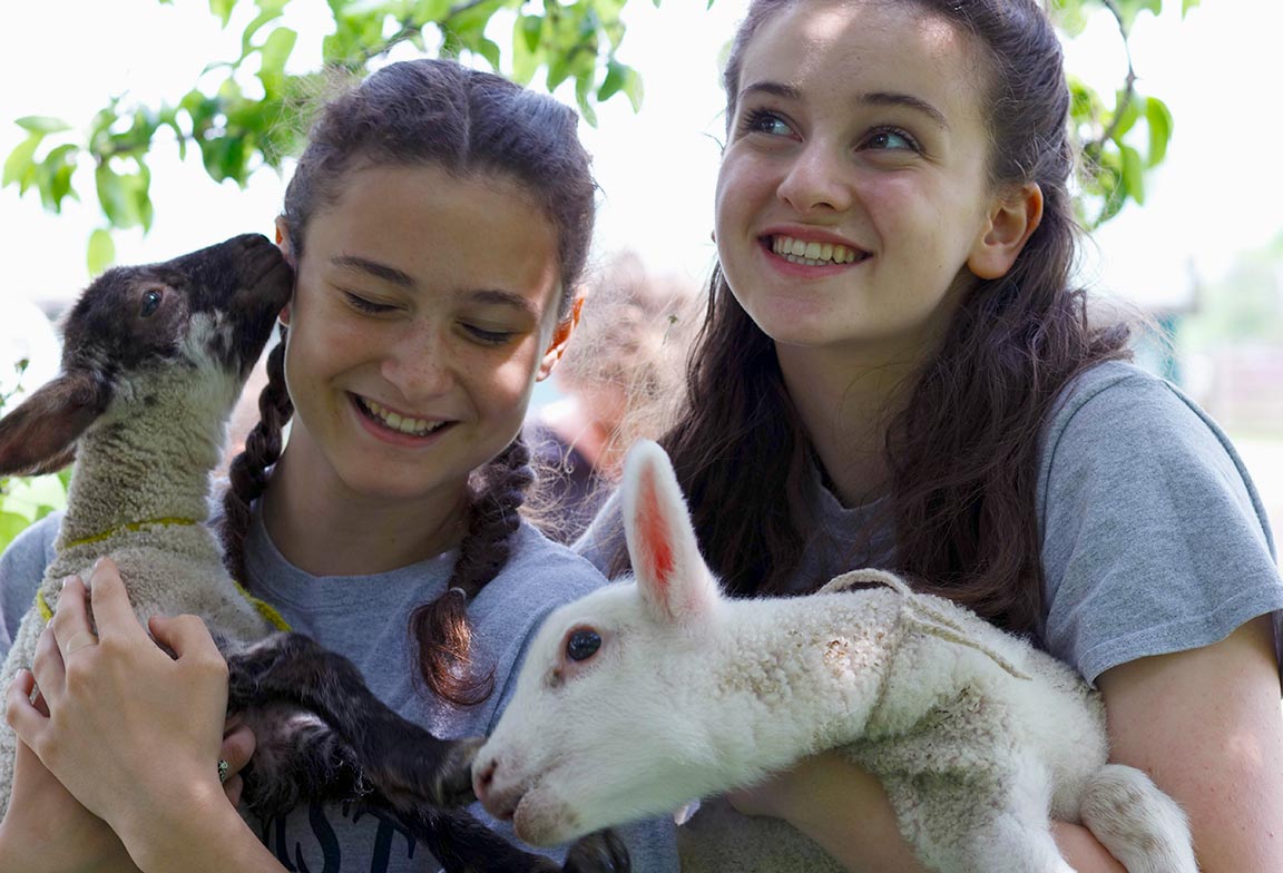 Picture of two students holding sheep during an outdoor enrichment activity