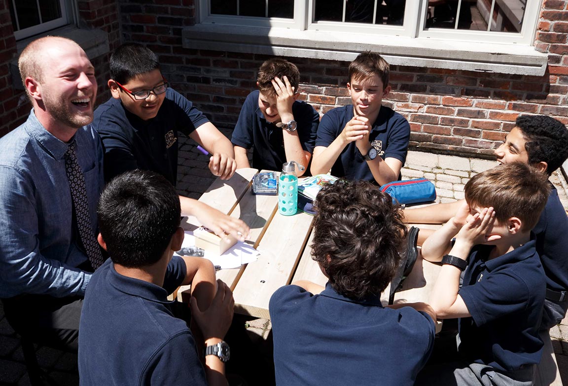 Picture of a teacher laughing with students during an outdoor class activity.