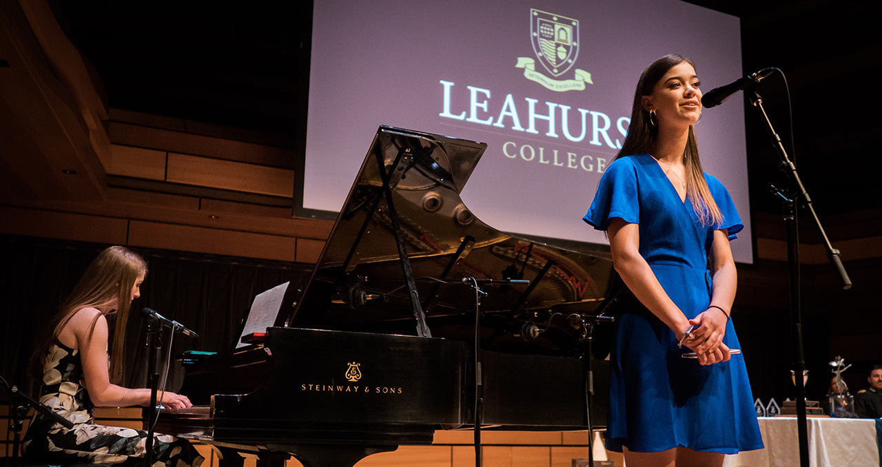 Picture of a student playing the piano while another student is singning on stage