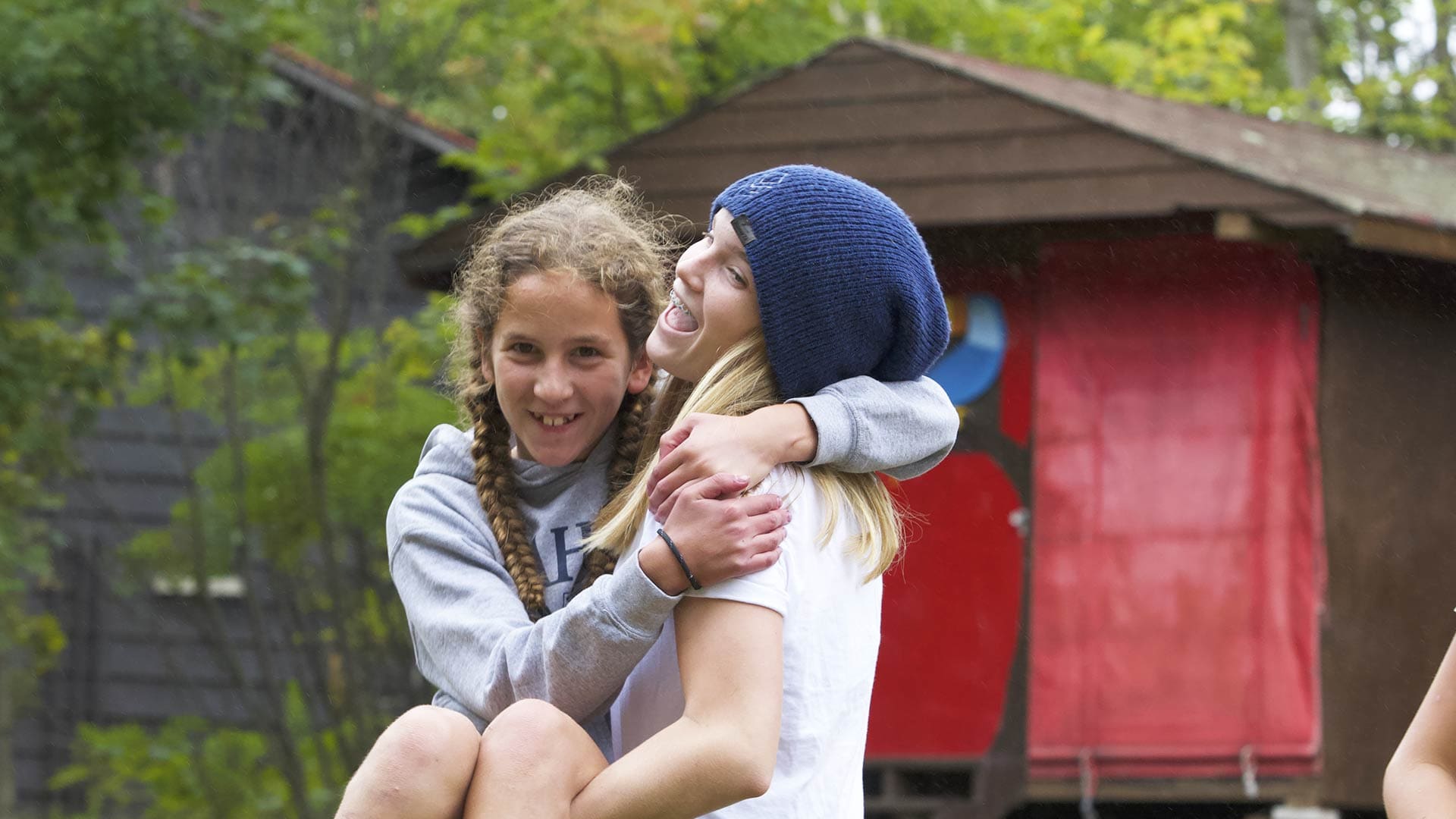 Picture of a student carrying another students in their arms and laughing while outdoors