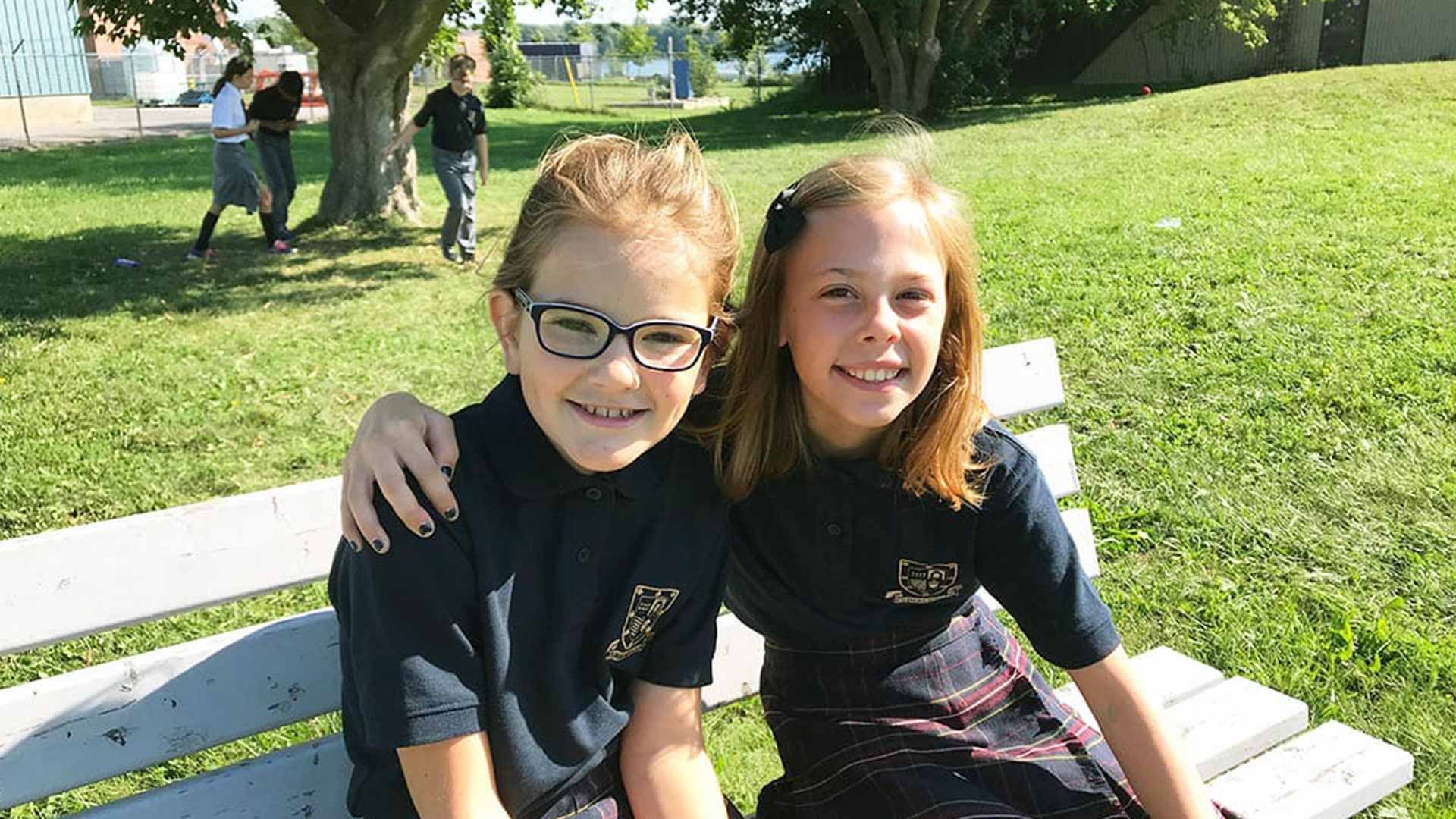 Picture of two students sitting on a bench outdoors and smiling