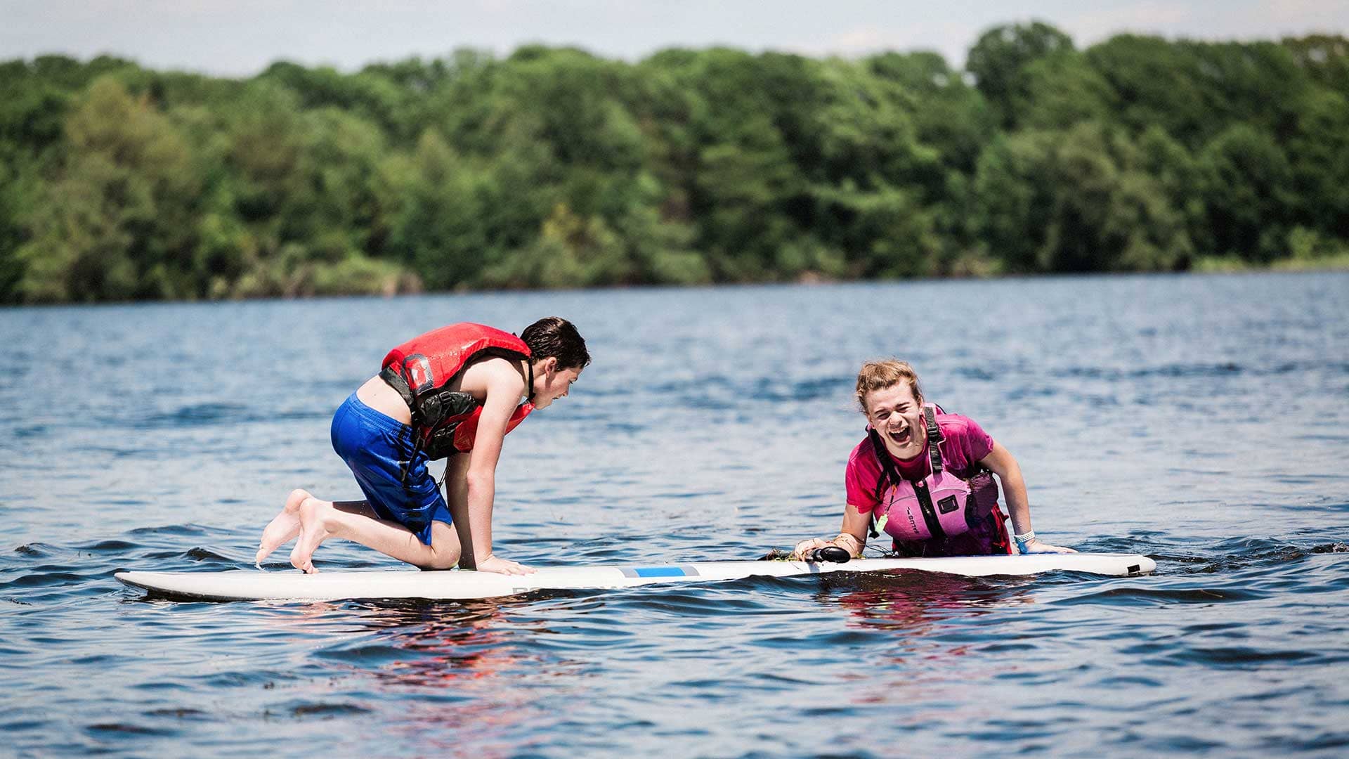 Picture of two students on paddle board on a lake and laughing