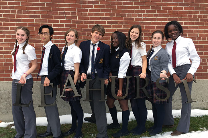 Picture of eight students outside in the winter posing for a photo while each holding metal letter that spell out Leahurst 