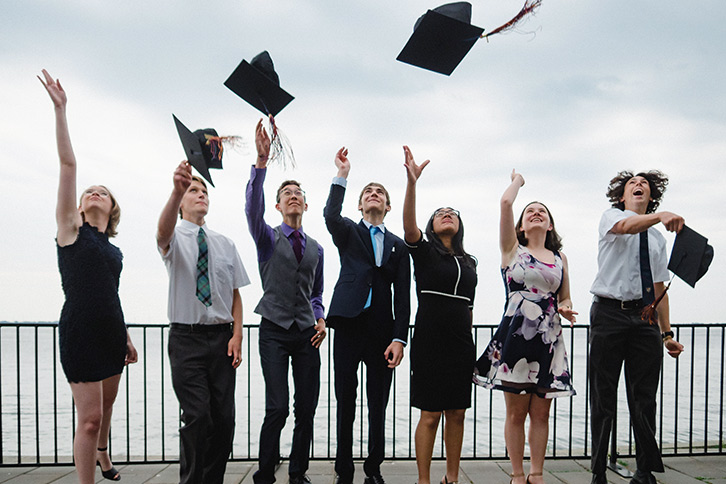 Picture seven senior school students outside of their graduating ceremony throwing their graduation caps into the air