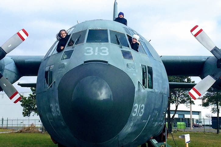 Picture of two students sitting in the cockpit of an grounded airplane and sticking their heads out for a photo during an enrichiment trip