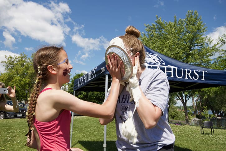 Picture of of a student throwing a pie in the face of another student during an outdoor House event