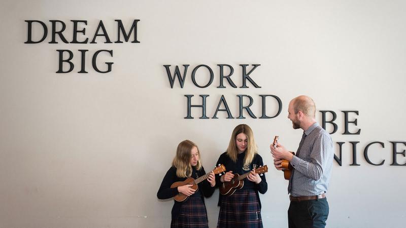 Picture of two student and a teacher playing the banjo
