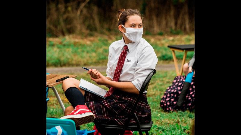 Picture of a student with a mask on sitting on a chair during an outdoor class