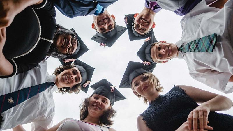Picture of students at graduation posing for a photo looking down at the camera on the floor
