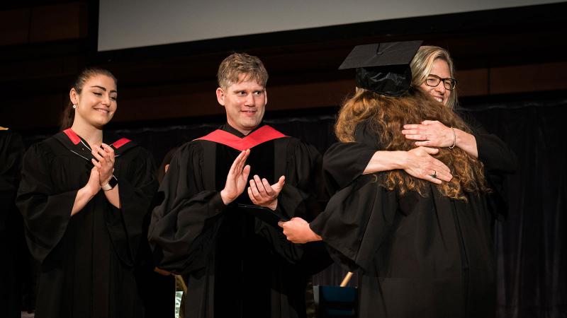 Picture of a teacher hugging a student and congratulating them when receiving their diploma of graduation