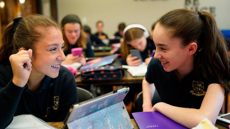 Picture of a classroom full of student with two students at the front looking at each other and smilling