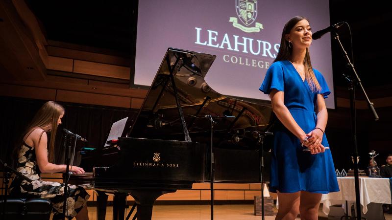 Picture of a music performance with a student playing the piano and a student signing