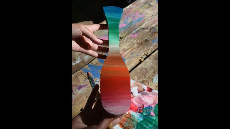 Picture of a student artwork in the shape of a paddle and painted in a red and green palette