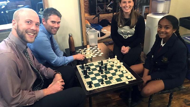 Picture of three teacher and a student sitting around a chess game