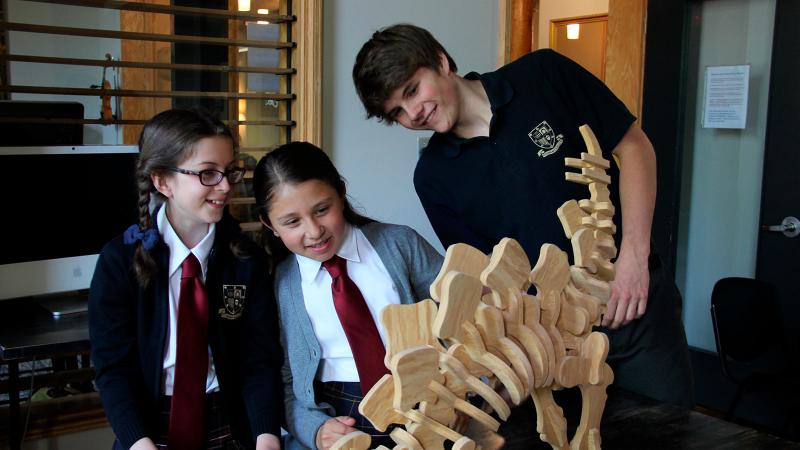 Picture of three students looking at a dinosaur skeleton made out of wood