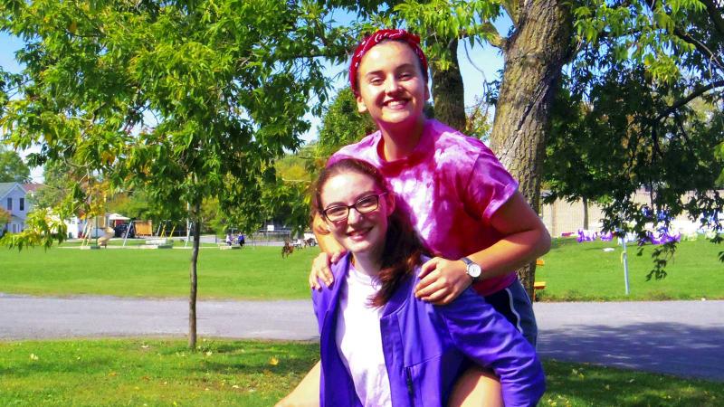 Picture of a student carying another student on their back outdoors