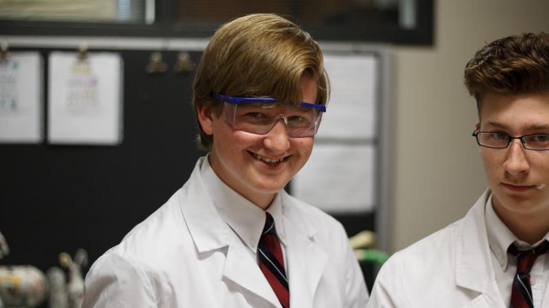 Picture of a student smiling in a lab coat in science class