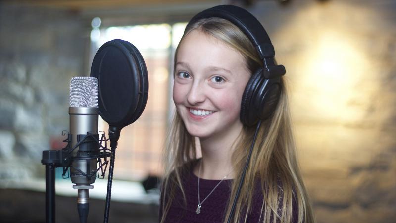 Picture of a smilling student recording her signing voice in front of a microphone