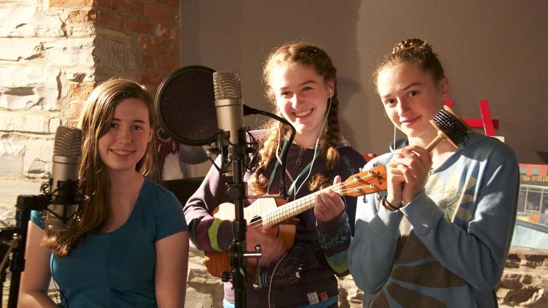 Picture of three student recording music in front of a microphone