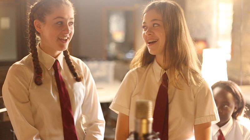 Picture of two students recording their a song in front of a microphone