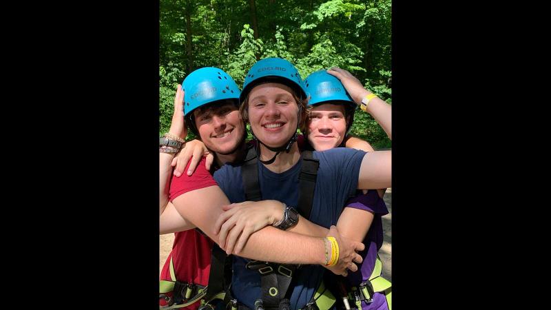 Picture of three students hugging for a photo and wearing their rock climbing helmets