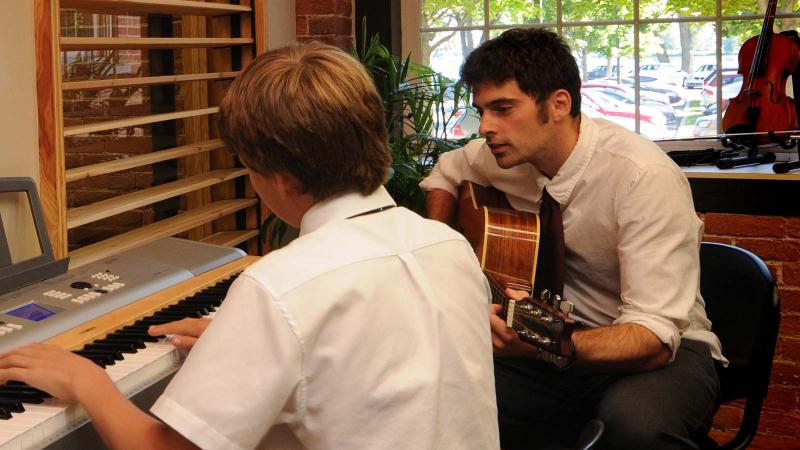 Picture of teacher playing the guitar and a student playing the piano