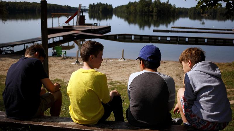 Picture of four students sitting on a log in front of a lake