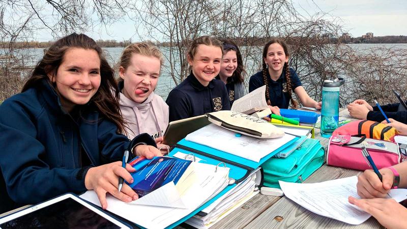 Picture of students sitting around a table in class working on school work outdoors