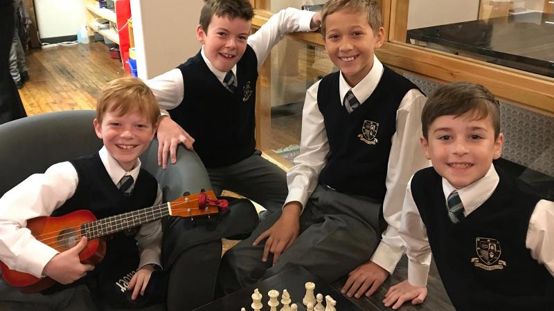 Picture of four students sitting around a chess board and one student holding a banjo