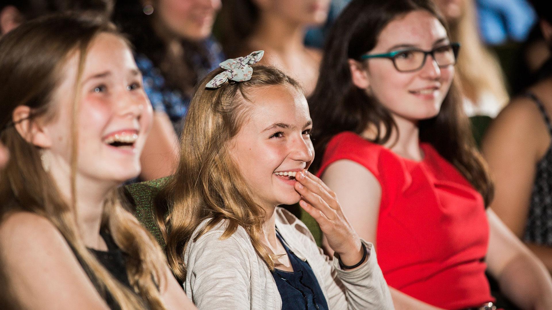 Picture of students in laughing while sitting in the audience at a graduation ceremony.